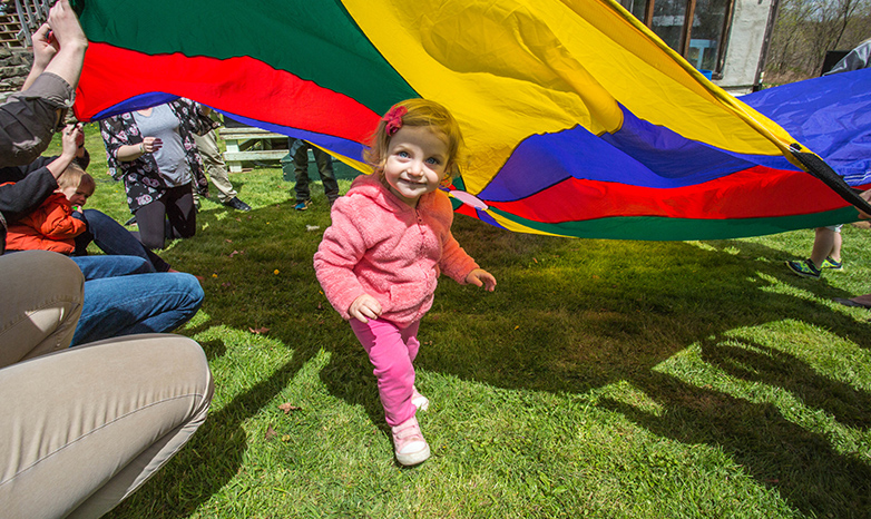 toddler running under colorful parachute during children's festival