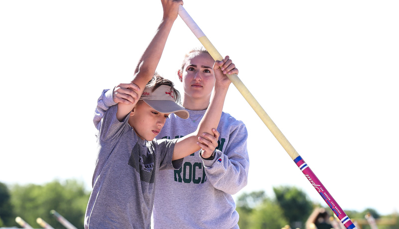 SRU student helps a high school athlethe with hand placement on a pole vault pole
