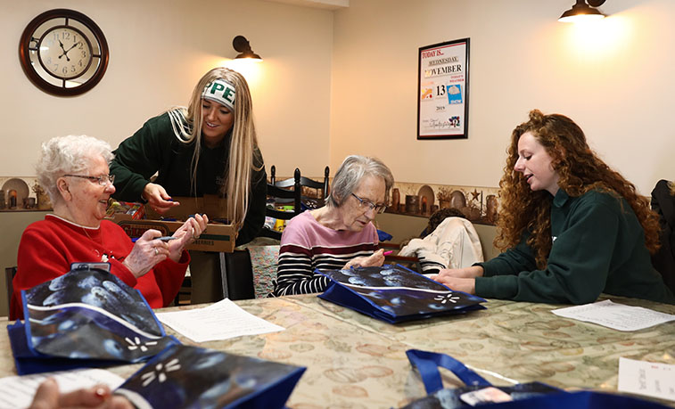 Second from left, Slippery Rock University students Gabrielle Cunningham and, far right, Rosemary Franklin help residents at the Home 2 Me assisted-living facility in Slippery Rock gather items for care packages that will be distributed to homeless people in Pittsburgh.