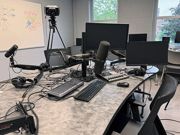 An image depicting a long and narrow desk with two microphone set ups sat across from each other.