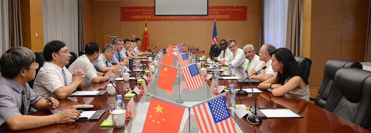 Signing Ceremony. SRU representatives and China Representatives talking. Chinese and American flags are present.