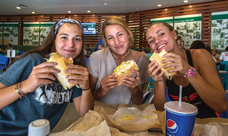 three students eating sub sandwiches