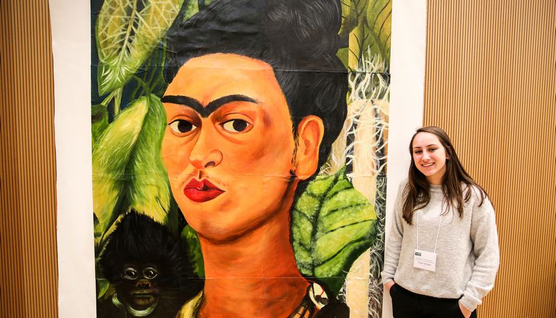 Student standing next to Frida Kahlo portrait
