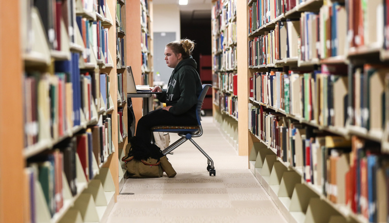 Woman reviewing material among the library book shelves