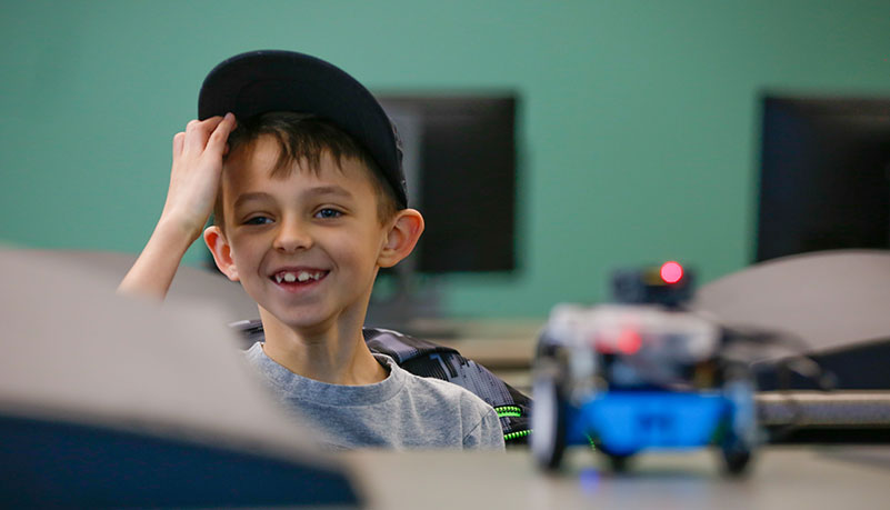 child with hat looking at robot