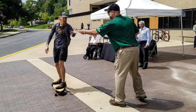 President handing put a snack bar to a student on a skateboard