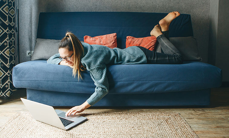 Student laying on a couch using a laptop