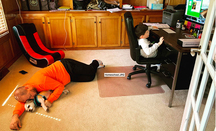 a dad lays on the floor while his son does school work on a computer