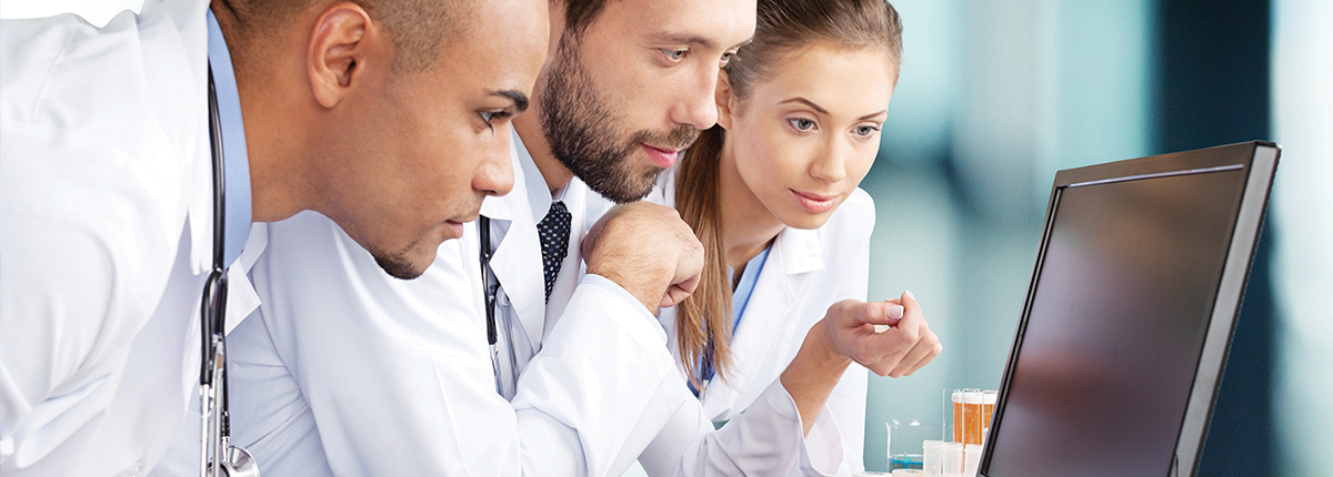 Three people in lab coats looking at a computer.