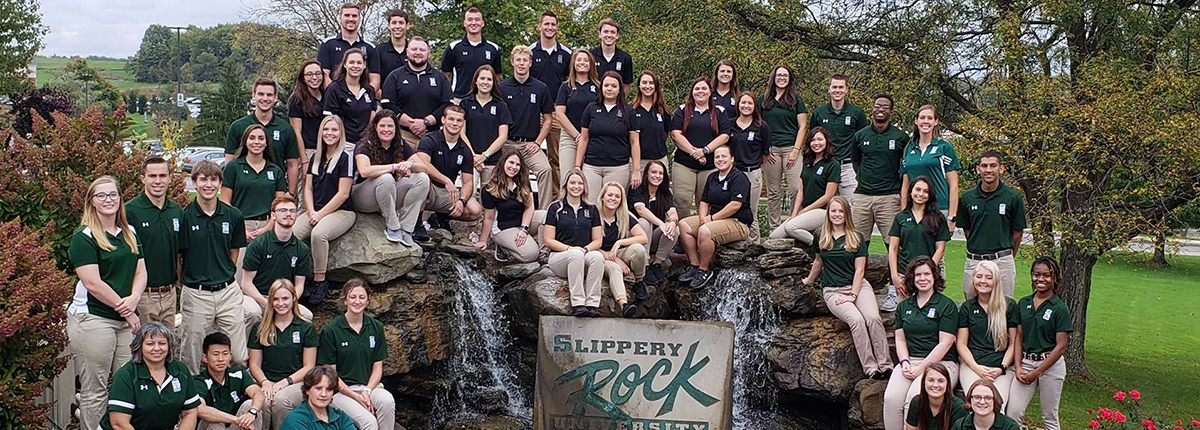 A group of SRU athletic trainers posing in front of the waterfall on campus
