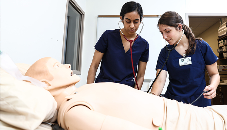 Two students with stethoscopes practicing on SIM man in the PA facility in Harrisville PA