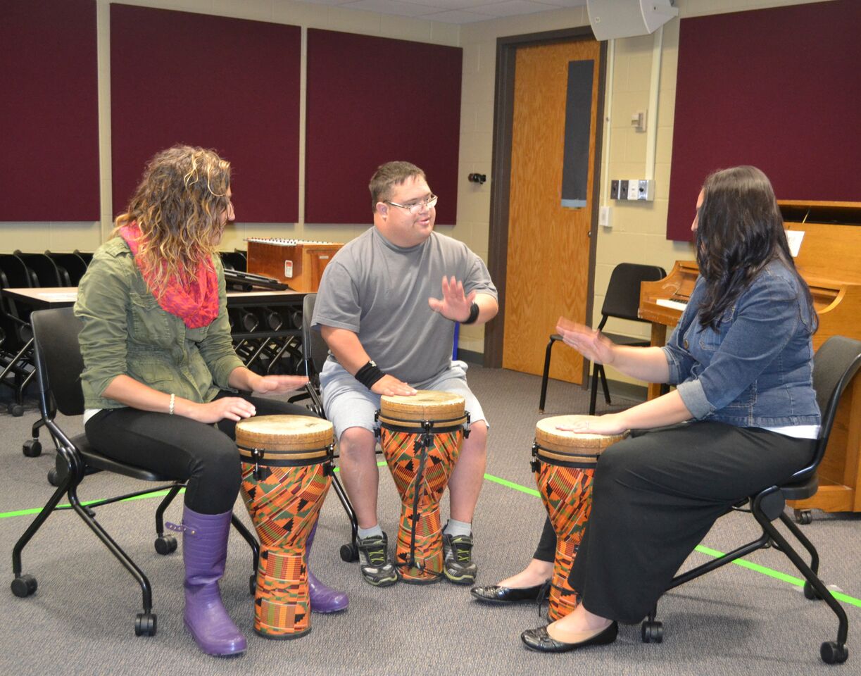SRU-MT-Clinic_Guitar-Drum.jpeg Music therapist playing guitar with boy on djembe drum