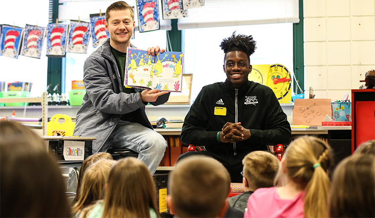 Football players reading to second graders