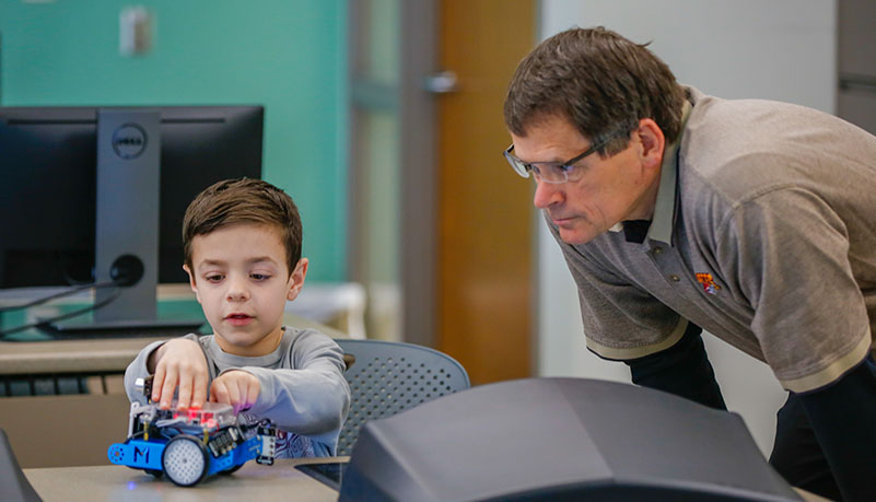 Professor watching child with a robot