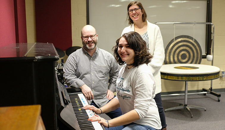 The music therapy staff and student at a piano